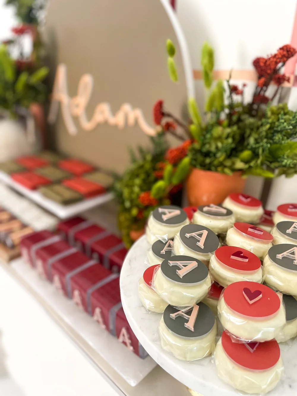 Iced biscuits marked with an A beside deep red favour boxes and greenery