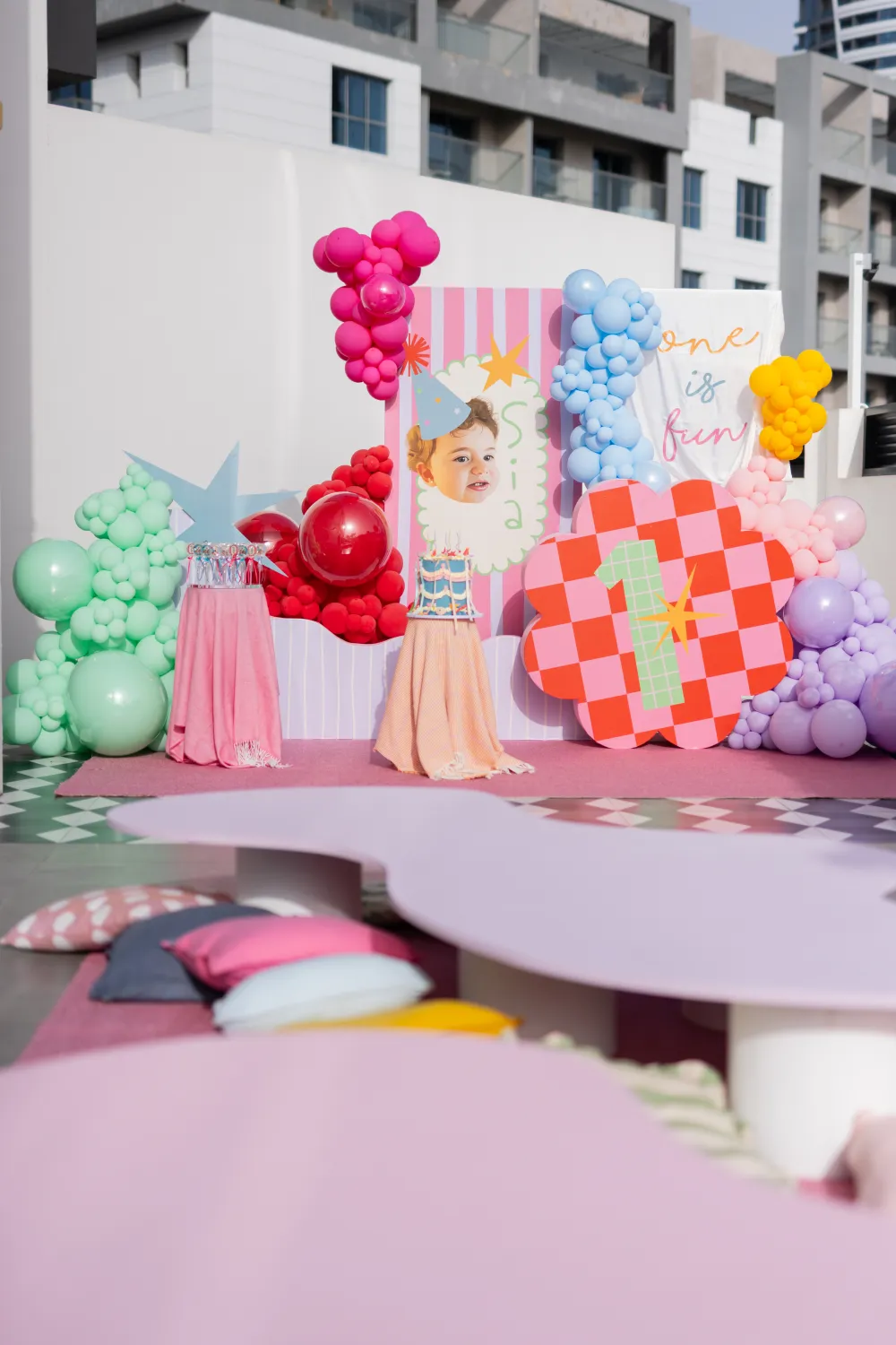 A colourful one of fun first birthday photo backdrop with bright balloons and a party hat motif