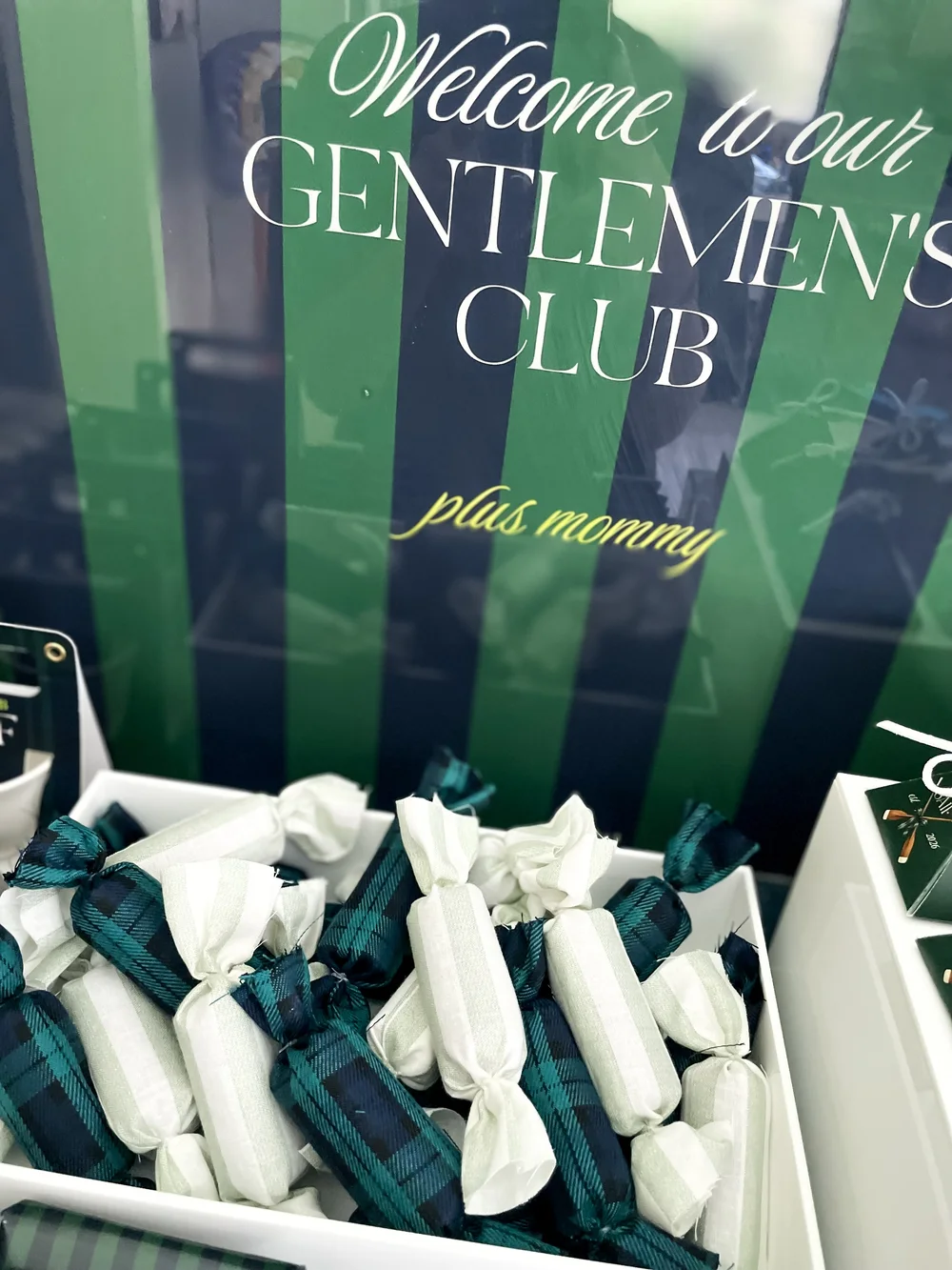 A welcome to our gentlemen's club sign in green and navy stripes above tartan wrapped favours