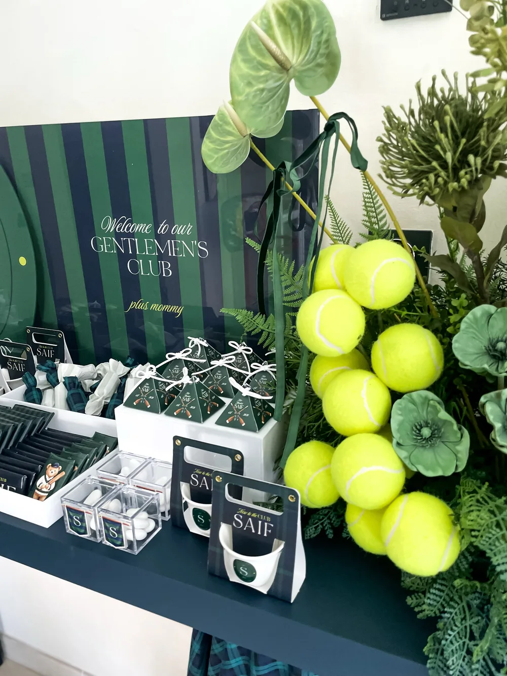 A gentlemen's club favour table with tennis balls, greenery and personalised boxes