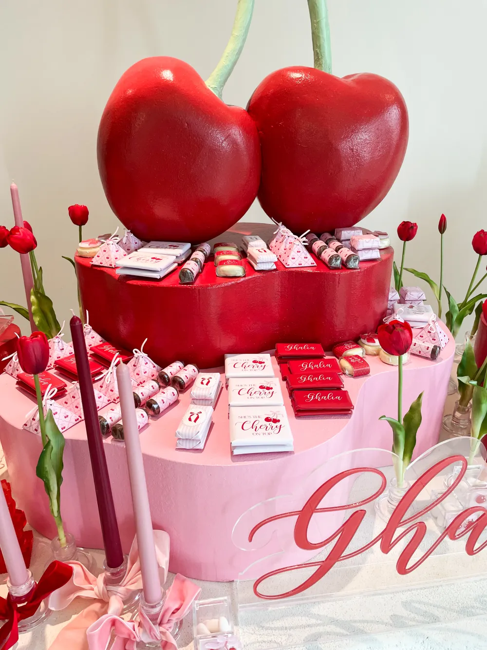 A red cherry themed newborn welcoming setup with chocolates and a giant cherry centrepiece