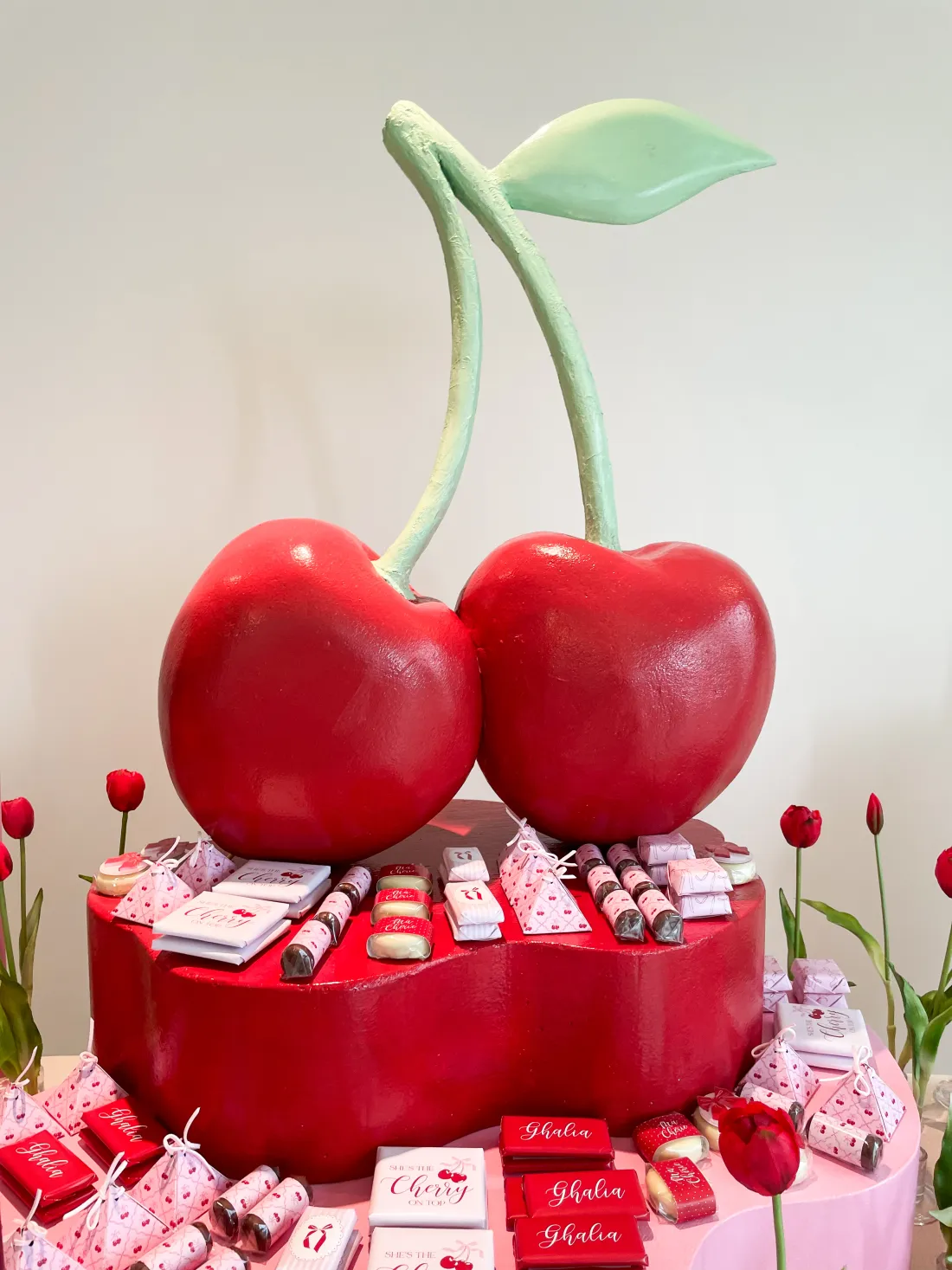 A bespoke red cherry themed newborn welcoming setup with a giant cherry centrepiece on a pink plinth and a personalised name display