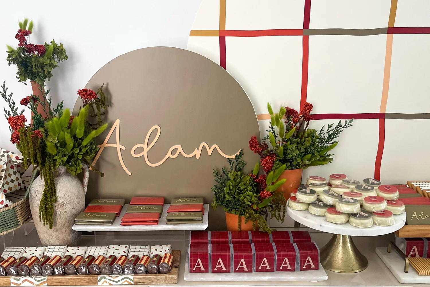 A newborn welcoming with a grid backdrop, a name arch and a dessert console in sage and deep red